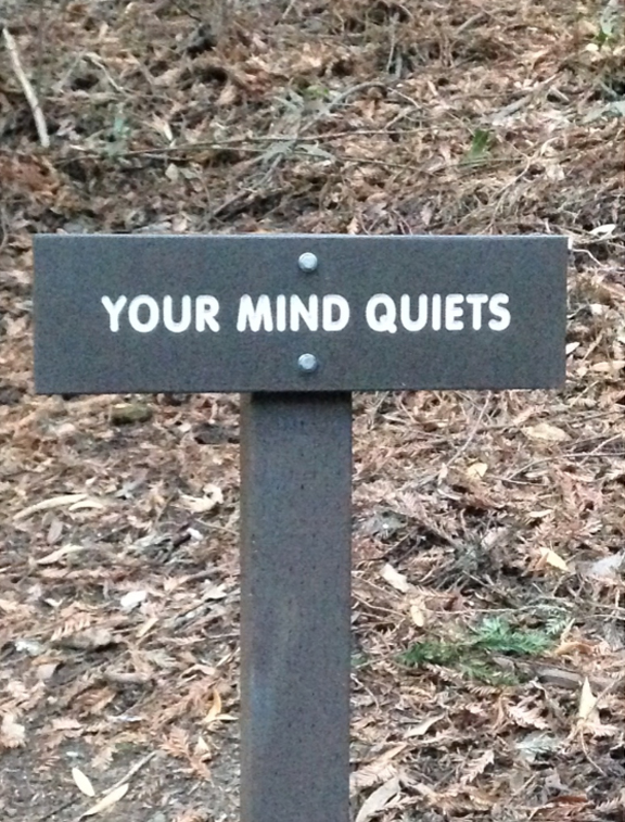 Trail sign reading 'Your Mind Quiets,' photographed outdoors as a reminder to unplug